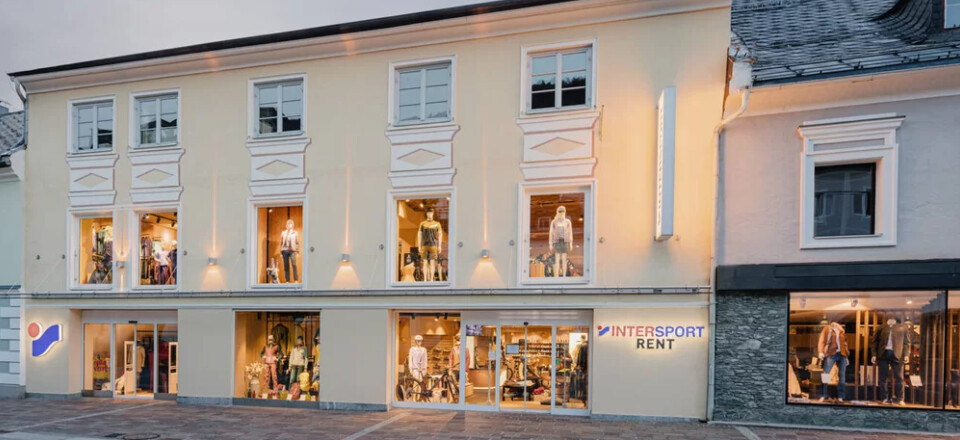 Two-story Intersport shop with illuminated windows displaying sports gear. The building is set in a quaint street with a calm evening ambiance.