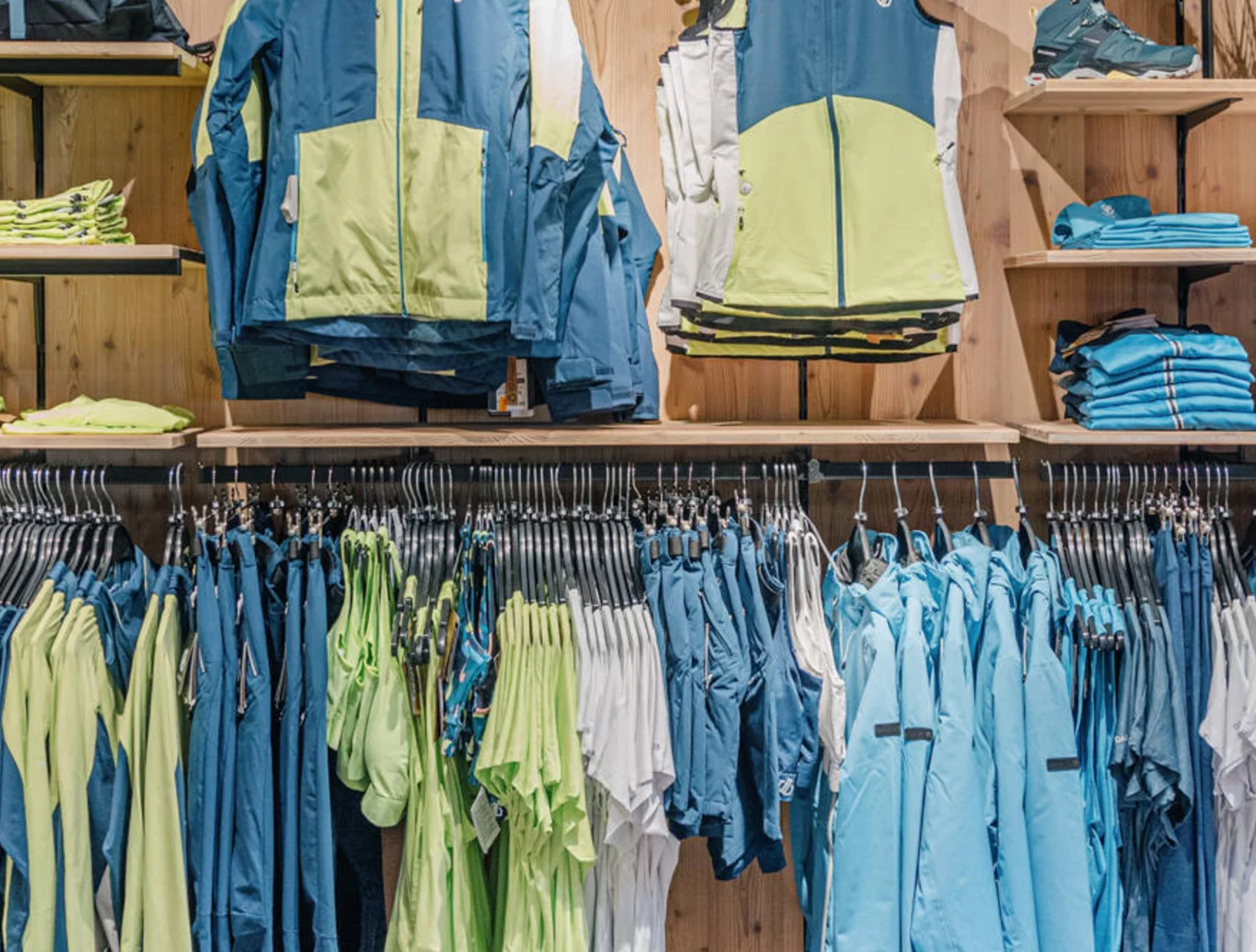 A clothing display features neatly arranged sportswear in blues and greens, including jackets, pants, and shirts, set against a wooden backdrop, conveying a sporty vibe.