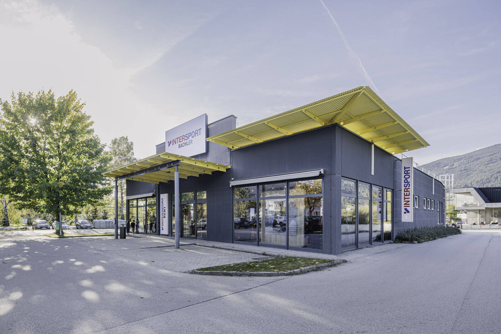 Modernes Intersport-Bachler-Gebäude mit gelbem Vordach und großen Glasfronten in sonniger Umgebung