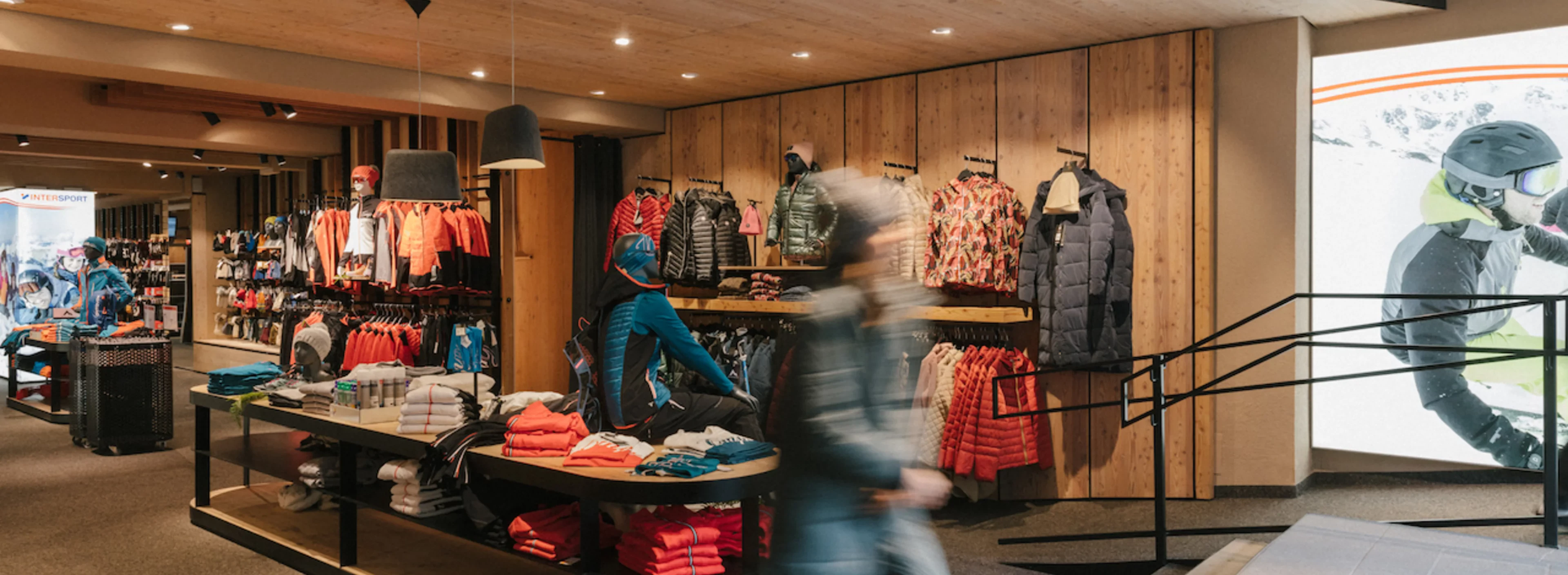A retail store interior with colorful clothing on racks and mannequins. A person walks by, creating motion blur. The atmosphere is vibrant and inviting.