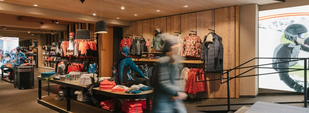 A retail store interior with colorful clothing on racks and mannequins. A person walks by, creating motion blur. The atmosphere is vibrant and inviting.
